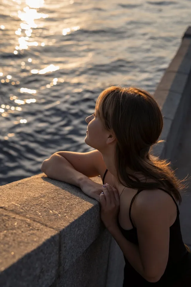 ノースリーブの女性が海と夕日を眺めているシーン