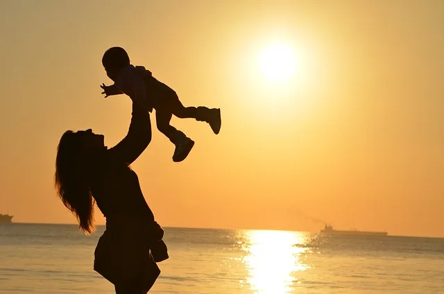 母親が子供を高く持ち上げて夕日を浴びている画像